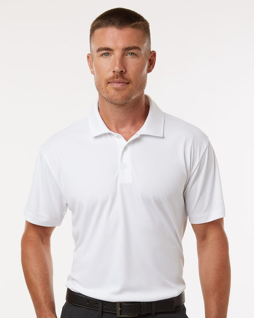 A man wearing a white short-sleeve polo shirt with a classic collar and button placket, paired with black trousers and a black belt, photographed against a clean white studio background.